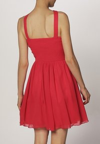 Red dress with a smocked bodice, thin straps, and a flowing skirt. Made of lightweight fabric with a smooth texture.