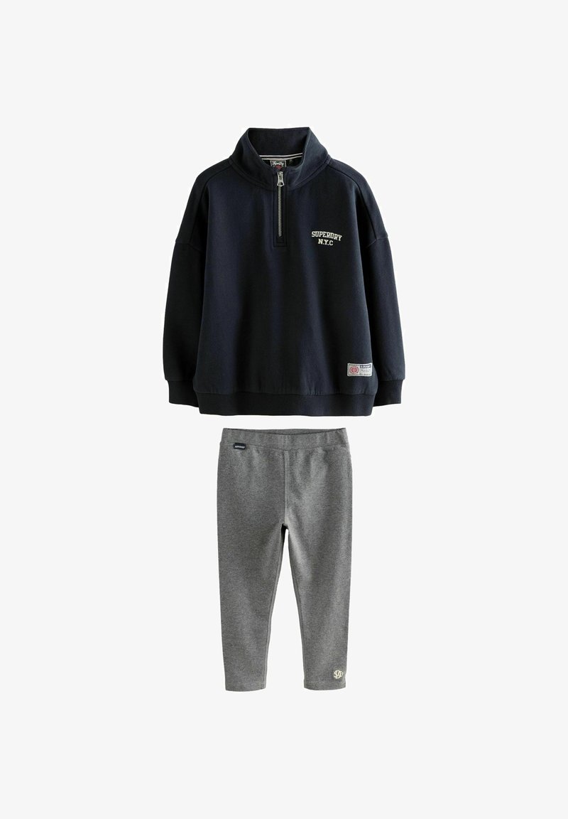 Sudadera de cremallera de un cuarto en azul marino con el texto "Superdry NYC" combinada con leggings ajustados grises, ambos son prendas de vestir casuales.