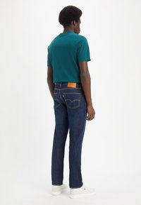 Teal kortermet t-skjorte kombinert med mørkeblå rette jeans, med en lærpatch på baksiden av livet og hvite joggesko.