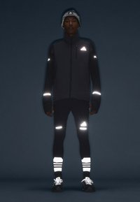 Black athletic jacket and leggings with reflective accents, textured beanie, and striped reflective socks. Features Adidas logo.