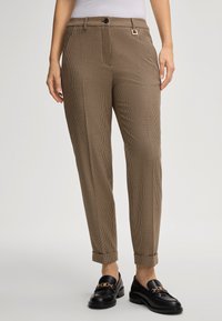 Pantalon à carreaux marron avec une coupe décontractée, comportant une fermeture à bouton, des passants de ceinture et des poignets retroussés, associé à des mocassins noirs.
