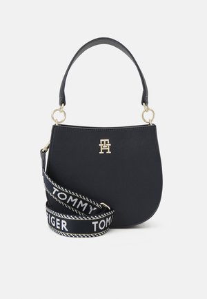 Navyfarbige Lederhandtasche mit geschwungener Form, goldener Hardware und abnehmbarem Tragegurt mit "TOMMY HILFIGER"-Muster.