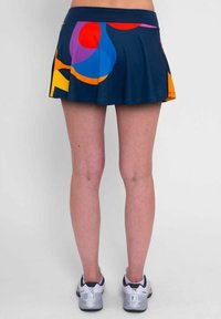 Una falda plisada de color azul marino con grandes patrones abstractos coloridos en rojo, naranja, púrpura y azul, combinada con zapatillas deportivas grises.