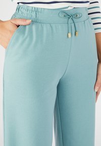 Lichtblauwe, broek met elastische tailleband en trekkoord, voorzien van zakken en een gladde textuur. Eenvoudig ontwerp zonder patronen of accenten.