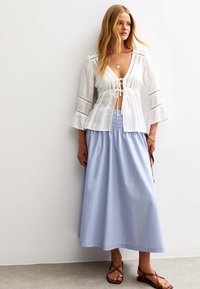 Vit linnblus med trumpetärmar och spetsdetaljer, tillsammans med en ljusblå maxikjol. Bruna sandaler med ankelrem fulländar outfiten.