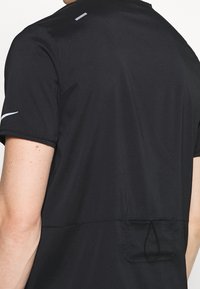 Černé sportovní tričko s texturovanou látkou, krátkými rukávy a malým reflexním akcentem na zádech pro lepší viditelnost.