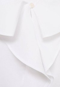 Valkoinen paita, jossa on suuri kaulus, napitus ja pehmeä, teksturoitu kangas. Suunnittelussa on kerroksellisia etuosiota.