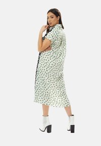 Green and white patterned dress with a collared shirt design, short sleeves, and a side slit, paired with white heeled ankle boots.