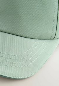 Casquette en tissu texturé vert clair, avec une visière courbée et des détails de couture proéminents. Profil lisse et structuré.