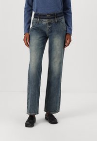 Wide-leg denim jeans in a faded blue wash, featuring a high waist, five-pocket design, and contrast stitching details. Paired with black loafers.