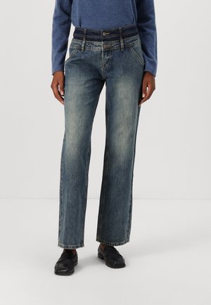 Vide bened jeans i en falmet blå vask, med høj talje, fem-lomme design og kontrastbroderi detaljer. Bærer sorte loafers.