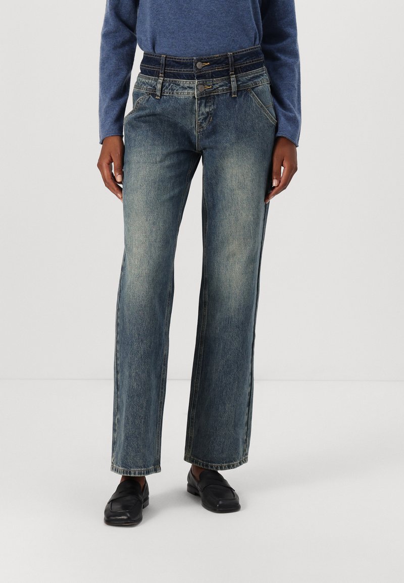 Wide-leg denim jeans in a faded blue wash, featuring a high waist, five-pocket design, and contrast stitching details. Paired with black loafers.