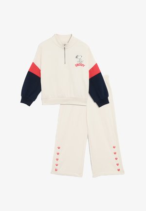 Cremefarvet træningsdragt med røde og marineblå accenter, der har en kvart-zip top med et Snoopy-grafik og bukser med hjerteformede knapper.