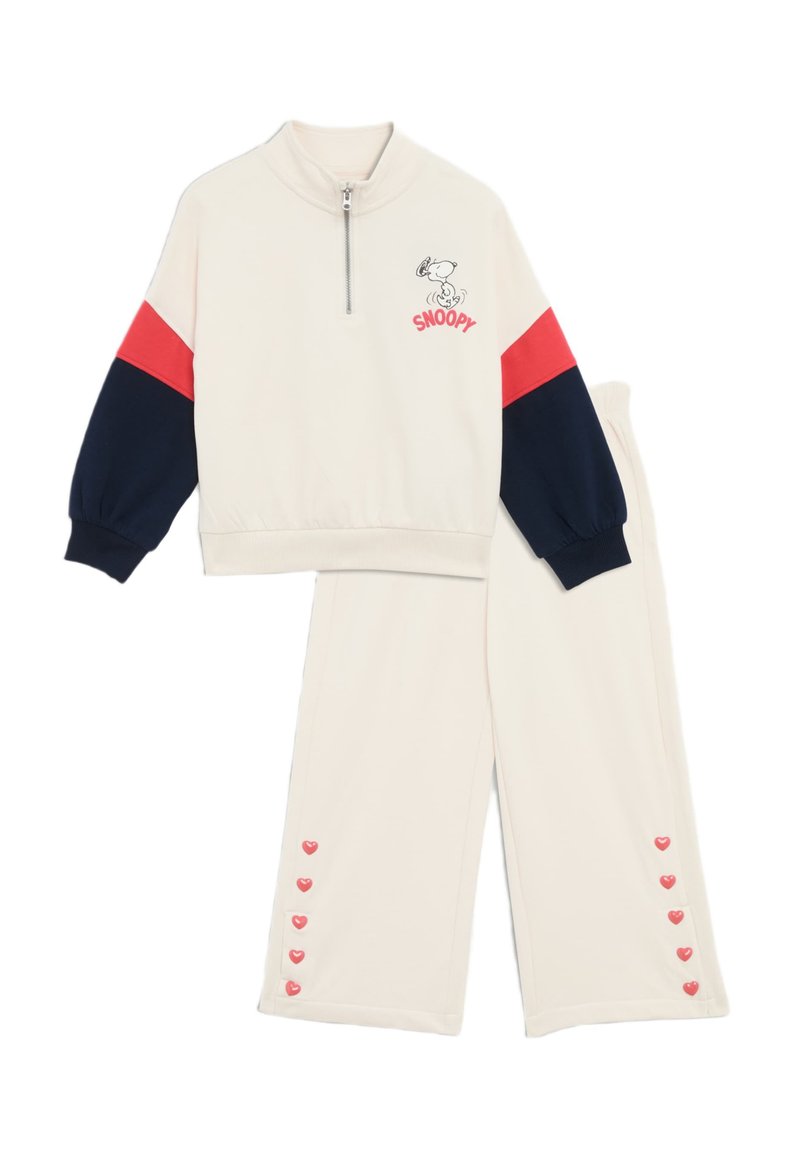 Survêtement crème avec des accents rouges et navy, comprenant un haut à zip quart avec un graphisme de Snoopy et un pantalon avec des boutons en forme de cœur.