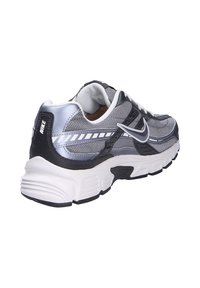 Scarpa sportiva argento e nera realizzata in materiali mesh e sintetici, con suola bianca chunky e logo Nike distintivo sul tallone.