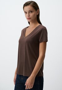 T-shirt marrone con scollo a V realizzato in un tessuto morbido e leggero, con maniche corte. Design aderente con una texture liscia e dettagli minimi.