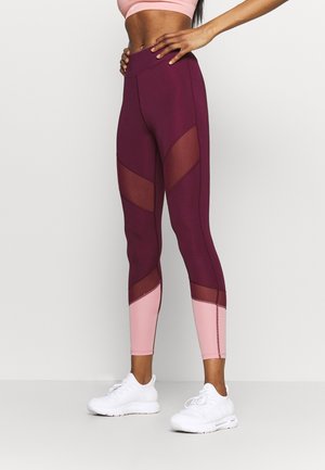 Athletic leggings in maroon and blush with mesh panels, high waist, form-fitting design, accent stitching, and finished hem.