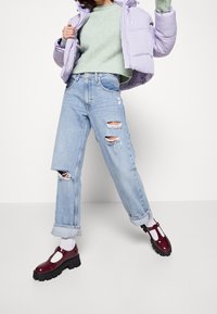 Wyściełana lawendowa kurtka, zielony sweter o fakturowanej strukturze, przetarte jasnoniebieskie jeansy oraz bordowe lakierowane buty na masywnych podeszwach z białymi akcentami.