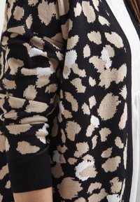 Cardigan nero con stampa leopardata in beige e bianco. Materiale in maglia textured con maniche a costine e design aperto.