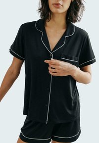 Czarna piżama z krótkim rękawem z białymi lamówkami, zapięciem na guziki oraz kieszonką na piersi, w zestawie z pasującymi szortami. Miękka struktura tkaniny.