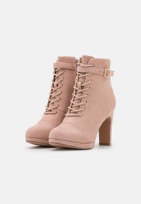Stivali alla caviglia in suede rosa con un design con lacci, zip laterale e un piccolo dettaglio con fibbia sulla cinghia. Tacco a stiletto, punta arrotondata.