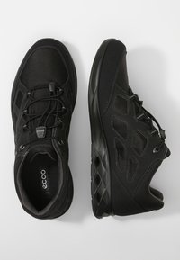 Černé atletické boty s texturovaným síťovaným svrškem, vyztuženou špičkou a flexibilní gumovou podrážkou. Vybaveny nastavovacími tkaničkami a diamantovým vzorem.