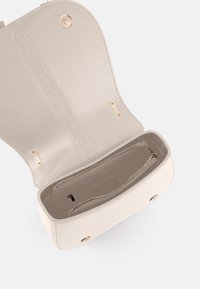 Sac à main en cuir beige clair avec un rabat arrondi, des ferrures dorées et une poche intérieure zippée. Texture lisse et design simple.