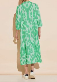 Zelené šaty s potiskem a vícero stupni, tříčtvrteční rukávy a staženým pasem. Nosené s bílými teniskami.