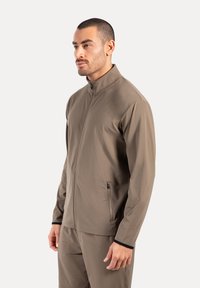 Herren braune Zip-Jacke aus glattem Stoff, mit hohem Kragen und seitlichen Reißverschlusstaschen, versehen mit schwarzen Akzenten an den Bündchen.