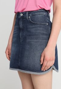 Jeans mini kjol i mörkblått med en lätt A-linjeform. Har en knappstängning fram, fickdetaljer och kontrasterande fållsöm.