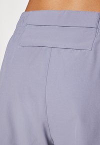 Calções atléticos lilás claros com uma cintura elástica e um bolso nas costas plano. O tecido tem uma textura suave e leve.