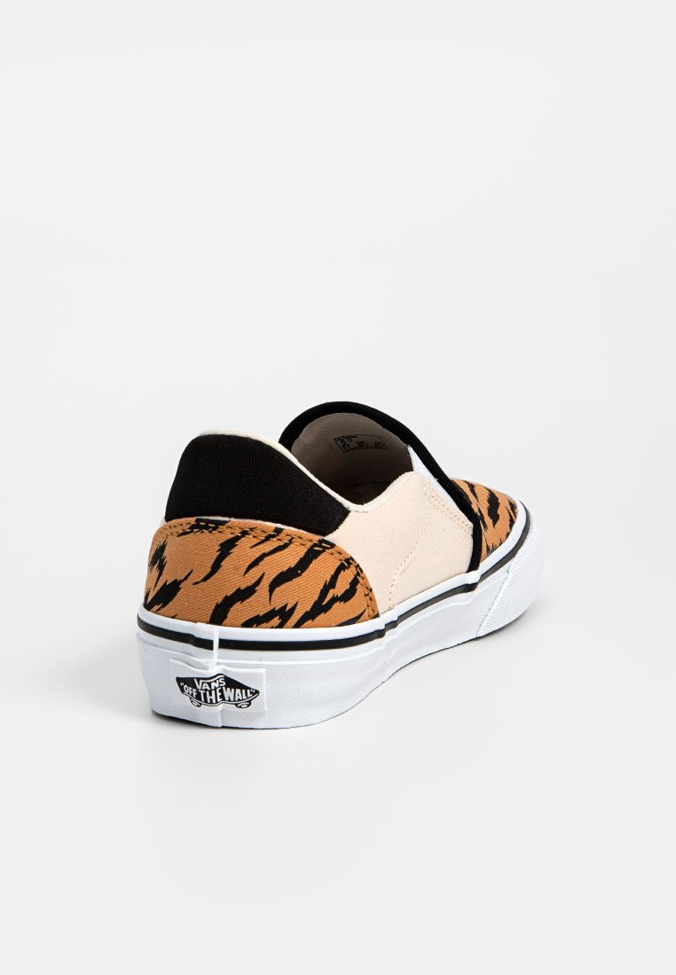Zapato tipo slip-on con un patrón de rayas de tigre en tono marrón y negro, parte superior de lona beige y acentos negros. Presenta una suela de goma blanca y detalle de logo.