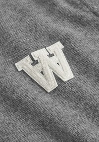 Gray fabric featuring an embroidered white "W" logo with a textured finish, set against a smooth knitted background.