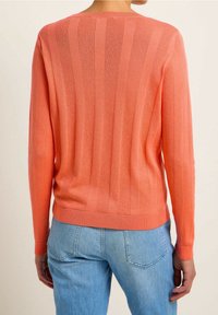 Coral-colored sweater with vertical ribbed texture, round neckline, long sleeves, and a fitted hem. Worn with light blue jeans.