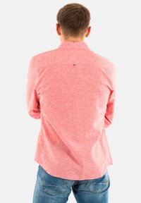 Chemise rose texturée à manches longues et à ourlet arrondi ; présente un petit logo au dos. Assortie avec un jean en denim bleu.