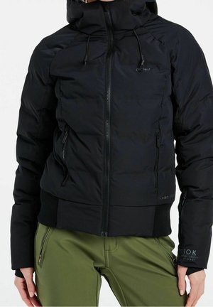 Persoon draagt een zwarte donsjas met ritssluiting aan de voorkant en een capuchon met trekkoorden, gecombineerd met olijfgroene broek met ritssluitingen op de zakken.