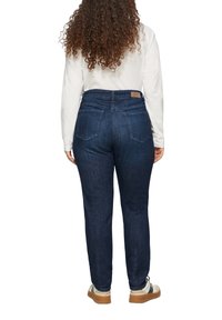 Ciemnoniebieskie dżinsy z wysokim stanem, z dwoma tylnymi kieszeniami i brązową skórzaną naszywką z logo marki na pasku.