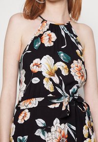 Robe noire à motif floral avec un col noué derrière le cou, ornée de fleurs orange et jaunes, d'accents feuillus et d'un détail de taille nouée.