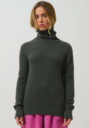 Dunkelgrüner, gerippter Rollkragenpullover mit langen Ärmeln und taillierten Bündchen. Weiches, strukturiertes Strickmaterial. Über einem pinkfarbenen, geschichteten Kleidungsstück getragen.
