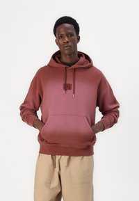 Maroon hoodie with a front pocket, drawstring hood, and small logo detail. Made from soft fabric with ribbed cuffs and hem.