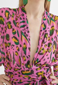 Rosa tyg med ett djärvt leopardmönster i grön, gul och svart. Har en djup V-ringning och en knytning i midjan.