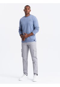 Lichtblauwe crewneck sweatshirt met een klein logo, gecombineerd met lichtgrijze cargobroek met zijzakken en witte sneakers.