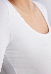Witte lange mouwen top met een ronde halslijn, gemaakt van zachte, rekbare stof met een gladde textuur, die de contours van het lichaam benadrukt.
