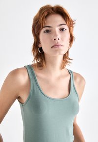 Lys grønn, ermeløs tank topp med rund hals. Glatt stoff med en figursydd design, som har brede skulderstropper.