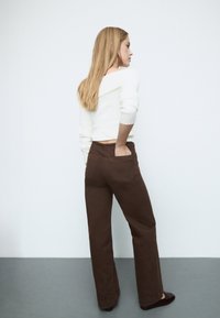 White cropped sweater with ribbed texture paired with brown wide-leg trousers; model's hands in pockets; flat black shoes.