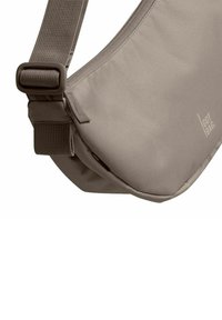Borsa a spalla beige con finitura in tessuto morbido, tracolla regolabile e dettaglio del logo del brand. Presenta una chiusura sicura per la regolazione della tracolla.