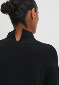 Pullover nero con colletto alto caratterizzato da un design a spacco sul retro. Il tessuto sembra liscio con una silhouette aderente e una texture a coste.