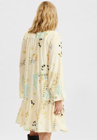 Šaty s květinovým vzorem v pastelově žluté barvě, s dlouhými rukávy a vrstveným lemem. Vyrobeny z lehkého materiálu; mají různé barevné botanické designy.
