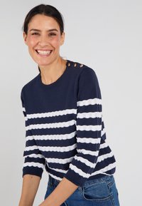 Pullover a righe blu navy e bianche, con maniche a tre quarti, caratterizzato da una trama simile pizzo e tre bottoni decorativi sulla spalla.