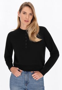 Pulover negru cu guler rotund, mâneci lungi și o bătătură cu cinci butoane negre. Purtați-l cu blugi cu talie înaltă, de culoare albastră.